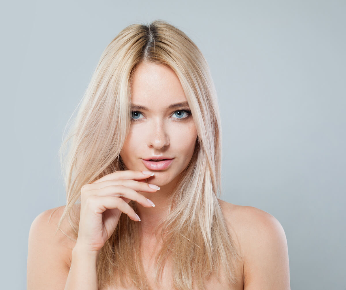 Lovely woman face close-up. Blonde model with fresh clear skin and healthy silky hair on white background